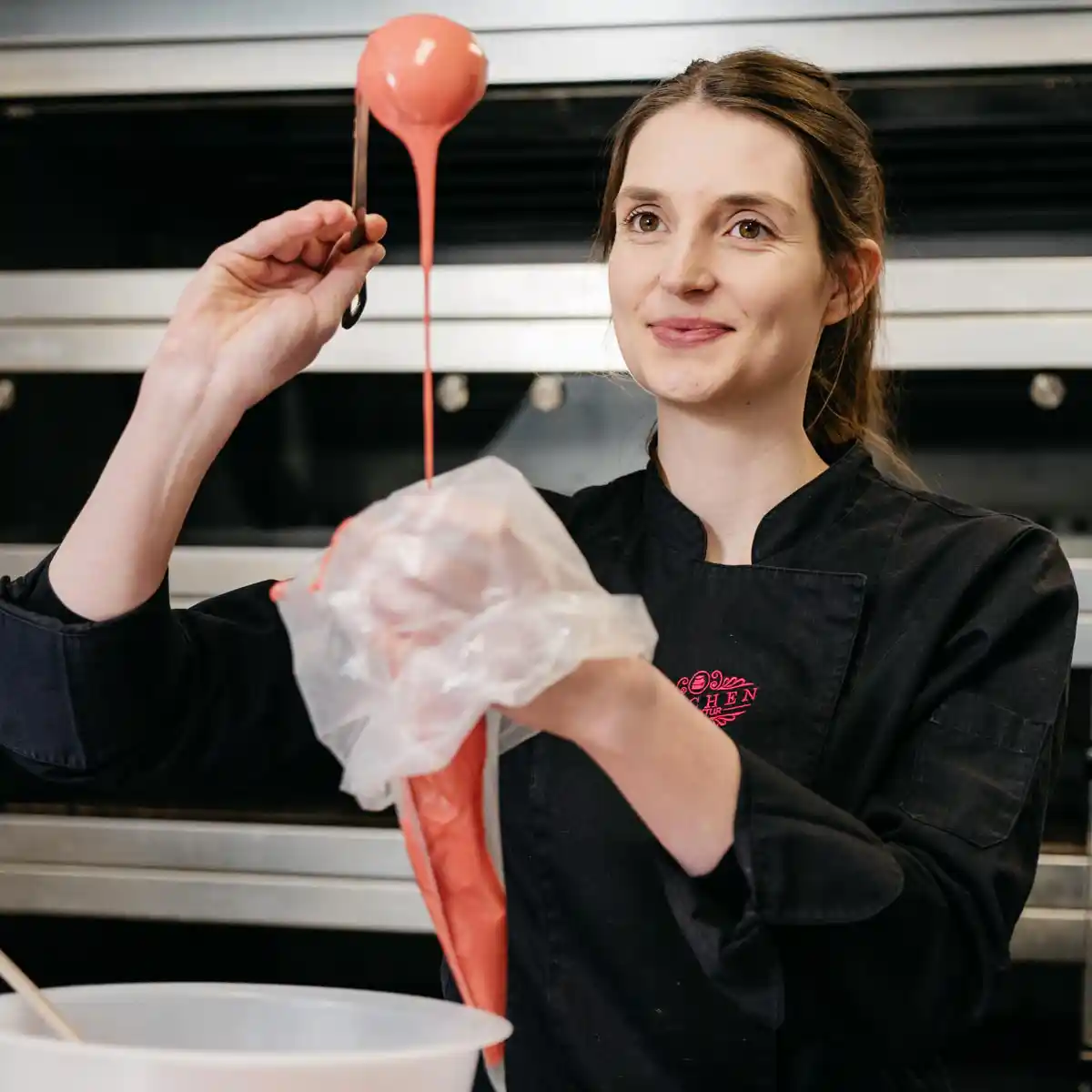Herstellung handgemachter Schokolade in der 7 Sachen Manufaktur Steinhagen – eine Mitarbeiterin füllt rosa Schokoladenmasse mit Sorgfalt in einen Spritzbeutel.