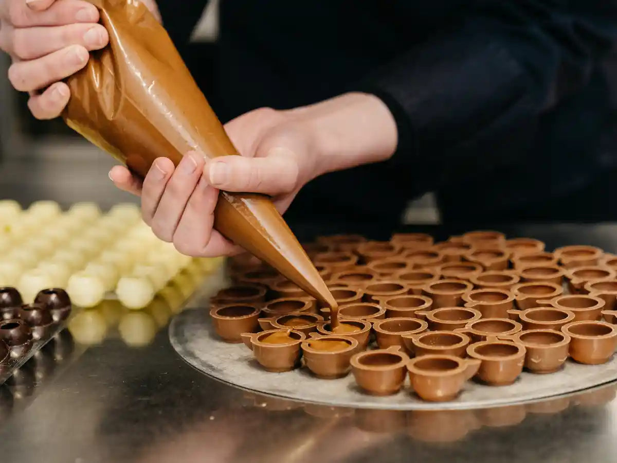 Herstellung handgegossener Pralinen in der 7 Sachen Manufaktur: eine Person füllt Schokoladenhohlkörper mit cremiger Füllung.