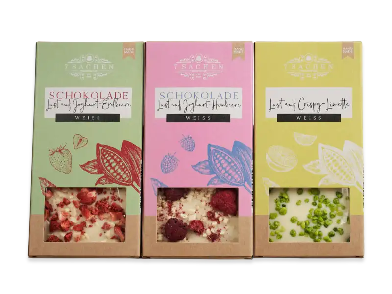 Drei Sorten weiße Schokoladentafeln von 7 Sachen Manufaktur – Erdbeere, Himbeere und Crispy Limette – in bunten Verpackungen mit Sichtfenster.